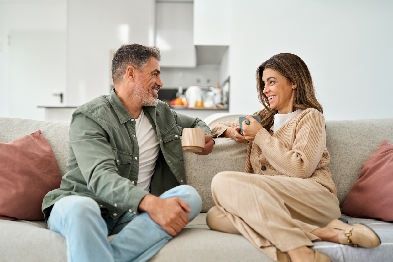 Happy middle aged mature couple talking relaxing on couch at home.